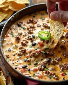 a hand dipping a tortilla chip into a bowl of chili cheese dip