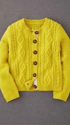 a yellow cardigan sweater with buttons on the front and bottom, sitting on a gray surface