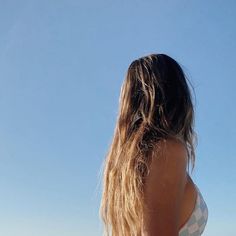 a woman standing on the beach with her back to the camera and looking up at the sky