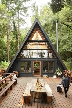 a - frame cabin in the woods with wooden decking and picnic table on it