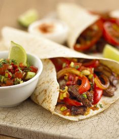 a tortilla filled with meat and vegetables on top of a wooden cutting board