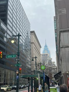 people are walking on the sidewalk in front of tall buildings and traffic lights with skyscrapers in the background