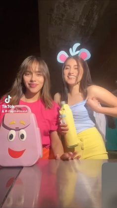 two girls are posing for the camera in front of a table with an object on it