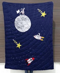 a person standing in front of a wall with a quilt on it that has space shuttles flying around the moon