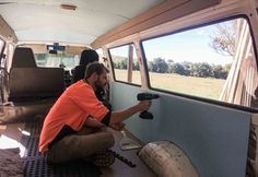 a man in an orange shirt is using a drill to paint the inside of a van