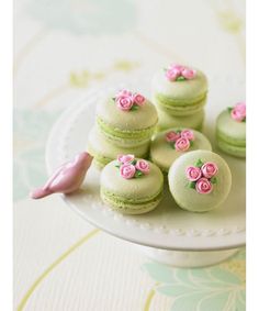 there are many green and pink macaroons on the cake platter with flowers