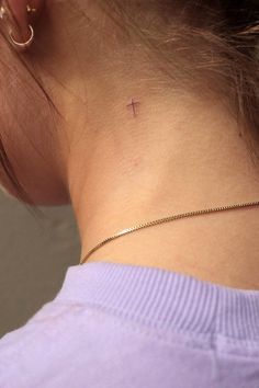 the back of a woman's neck with a cross tattoo on her left side