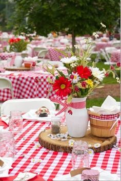 a red and white checkered table cloth with flowers in a vase on it,