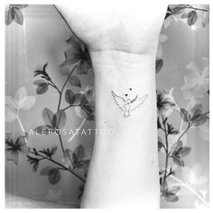 a black and white photo of a small tattoo on the left inner wrist, with an image of a bird flying above it