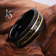 a black and gold wedding ring sitting on top of a piece of wood next to a rock