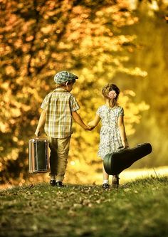 two children are holding hands and walking in the grass with suitcases on their feet