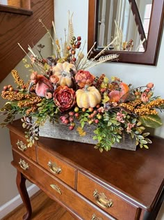 a wooden dresser topped with a vase filled with flowers and leaves next to a mirror