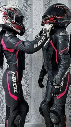 two people dressed in black and pink are standing next to each other with helmets on