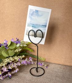 a photo frame on a stand next to flowers and a vase with purple flowers in it