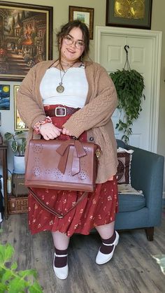 Plus sized brunette girl wearing white frilly top, long red orange floral print skirt, cozy tan cardigan, white maryjane shoes and a brown leather bag. Background has a variety of paintings, prints, and plants. Cottagecore Outfits Simple, Hippy Cottagecore Outfits, Artsy Outfit Ideas Plus Size, Super Plus Size Fashion, Cottage Core Outfit Plus Size, Clothing Aesthetic Plus Size, Whimsical Fashion Plus Size, Plus Size Hippie Clothes, Fem Cottagecore Outfits