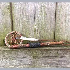 an old style dream catcher with feathers on it's back end sitting next to a wooden fence