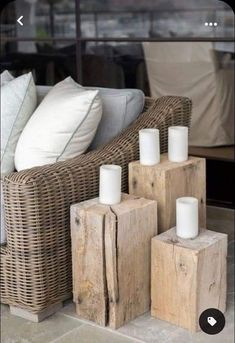 some candles are sitting on wooden blocks in front of a wicker couch with white pillows