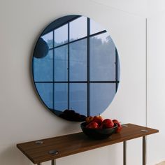 a bowl of fruit sitting on top of a table next to a window with a circular mirror above it