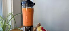 a blender filled with orange liquid sitting on top of a table next to a bowl of fruit