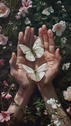 two hands are holding white butterflies in front of pink flowers and green leaves, while the other hand is reaching out towards them