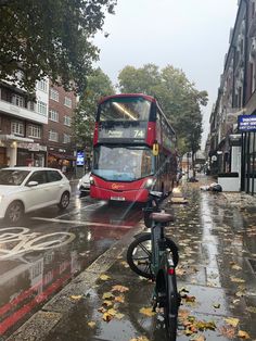 a red double decker bus driving down a rain soaked street