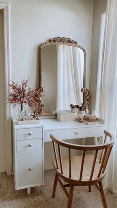 a white desk with a mirror, chair and vase on it in front of a window