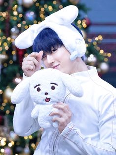 a person holding a stuffed animal in front of a christmas tree