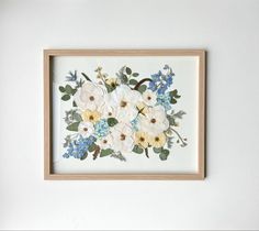 a white and blue flower arrangement is framed in a wooden frame on the wall above a bed