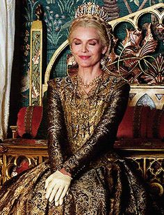 a woman sitting on top of a golden chair wearing a tiara and dress with gold sequins