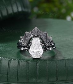 a close up of a ring with a diamond on the center and leaves around it