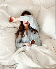 a woman is laying in bed with her eyes closed and holding a cup of coffee