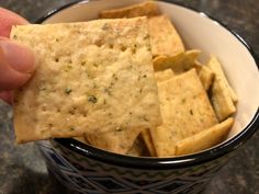 a hand holding a cracker over a bowl of chips