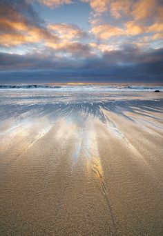 the beach is covered in sand and water under a colorful sky with clouds above it