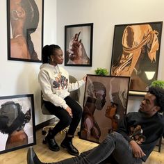 a man and woman sitting on the floor in front of some framed pictures with black women