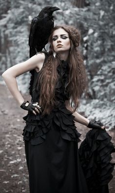 a woman with long hair wearing a black dress and holding a bird on her shoulder