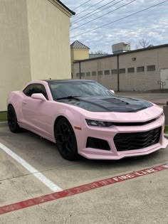 a pink chevrolet camaro is parked in a parking lot next to an empty building