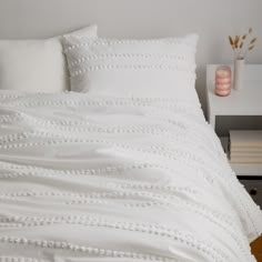 a bed with white sheets and pillows on top of it next to a night stand