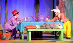 two people dressed as clowns sitting at a table with a baby on the ground