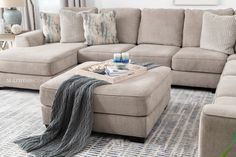 a couch and ottoman in a living room with pillows on the floor, blankets draped around it