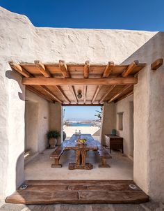 an outdoor dining area with wooden table and benches under a pergolated roof over looking the ocean