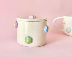 two white mugs with flowers on them sitting next to each other in front of a pink background