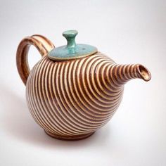 a ceramic teapot with a striped design on the outside and a blue top sitting on a white surface