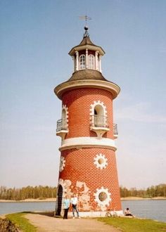 two people standing in front of a red and white tower next to the water on a sunny day