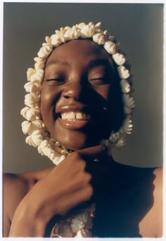 a woman with her eyes closed smiling and holding flowers in front of her face while wearing a headdress