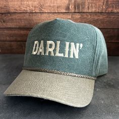 Vintage Style Darlin' Embroidered Faded Canvas Snapback Trucker Rope Hat with Free Shipping. White stitched text/logo. Condition is "New with tags". Shipped with USPS First Class. Step into the world of the great outdoors with our Darlin' Stitched Green Faded Canvas Rope Hat. With its faded canvas and rope accents, this hat exudes rustic charm and pays tribute to the iconic country music legends. Plus, enjoy free shipping on this vintage-inspired accessory that's perfect for any country music en Vintage Adjustable Hat In Faded Color, Vintage Adjustable Faded Hat, Faded Vintage Cap, Vintage Cotton Snapback Hat With Embroidered Logo, Vintage Snapback Hat With Letter Patch, Vintage Faded Cotton Baseball Cap, Vintage Cap With Letter Patch, Vintage Curved Bill Hat With Embroidered Logo, Vintage Hat With Letter Patch