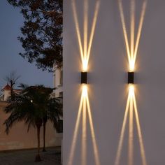 two wall lights on the side of a building with palm trees in front of them