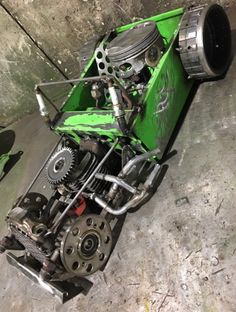 a green motorcycle engine sitting on top of a cement floor next to a metal object