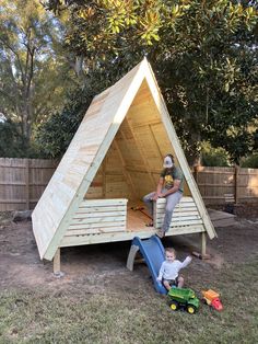 a woman and child playing in a wooden play house with a slide on the ground