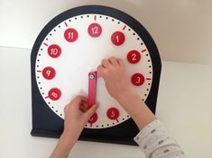 a child is playing with a clock that has red numbers on the face and hands