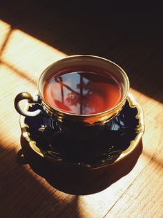 a cup of tea sitting on top of a wooden table next to a shadow cast window